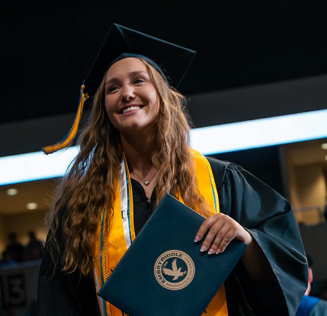 An Embry-Riddle graduate with various honors proudly receives her diploma at Commencement.